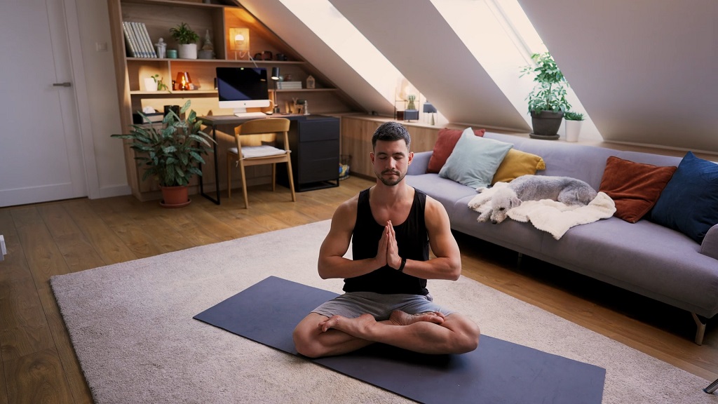 A man sitting cross-legged on a yoga mat in a peaceful attic room